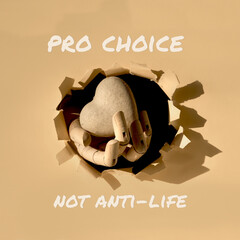 Text Pro Choice not Anti-Life. Cardboard heart in wooden model hand through paper hole in torn...