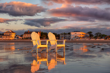 Two wooden traditional armchairs on a sandy beach at sunrise overlooking the coastline. Atlantic...