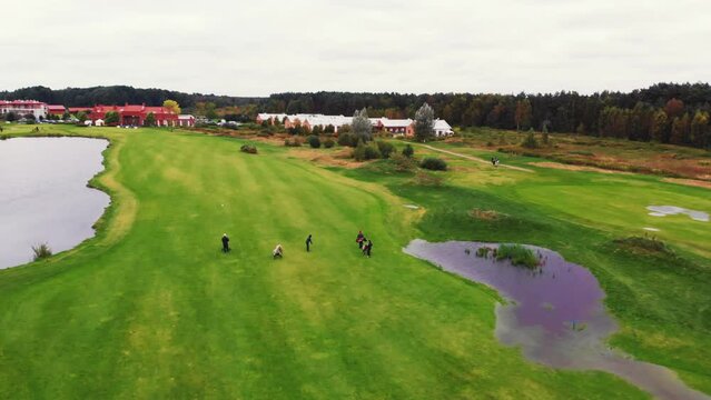 Wide aerial shot of a golf course in autumn. Green grass, big ponds, puddles and people with a professional golf equipment. High quality 4k footage