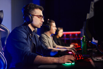 Side view portrait of young man playing video games with cyber sport team in background, copy space