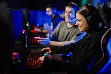 Side view portrait of smiling young woman playing video games on PC with cyber sport team cheering
