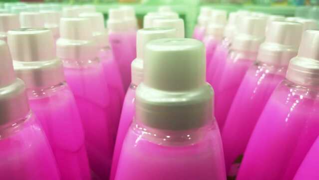Pink fabric softener in plastic bottles stand in rows on a shelf in a supermarket or in a warehouse