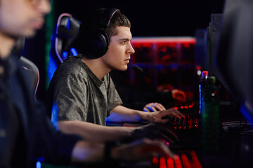 Side view portrait of focused young man playing video game with cyber sport team in dark