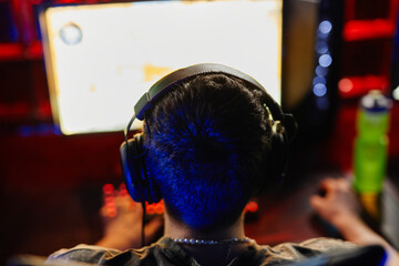 Obraz premium Back view at man playing video games in dark, focus on head with headphones, copy space