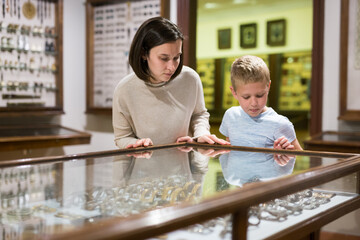 Young woman with son observing with interest exhibition under glass in art gallery