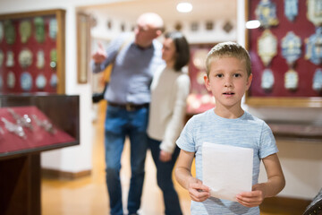 School boy looking exhibits at exposition in museum, man and woman standing on background