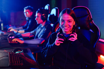Portrait of young woman on cyber sports team smiling at camera cheerfully lit by neon light, copy...