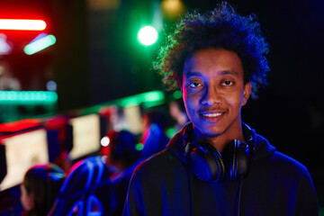 Portrait of black young man on cyber sports team smiling at camera lit by neon light, copy space