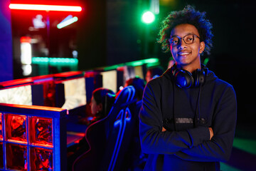 Waist up portrait of African American young man on cyber sports team smiling at camera lit by neon light, copy space