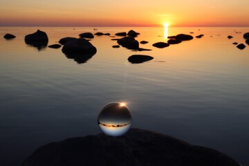 Crystal ball on rocky beach on a big gray granite boulder, sunset reflecting