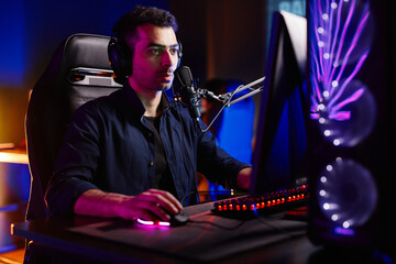 Portrait of young man playing video games in dark studio with neon accents streaming live