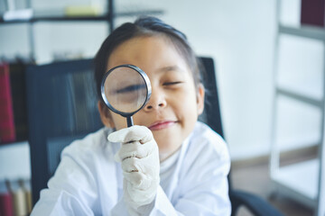 Little asia kids girl with magnifying glass in lab learning chemistry in school laboratory. Young...