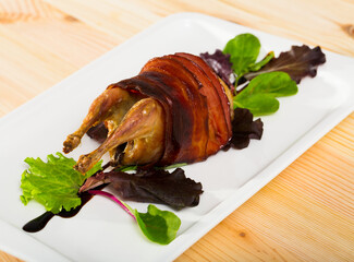 Wrapped in bacon baked quail served on plate seasoned with balsamic sauce
