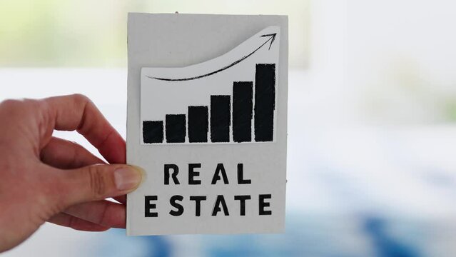 property value and return on investment or rent price, hand holding real estate sign with graph showing stats going up in front of living room bokeh