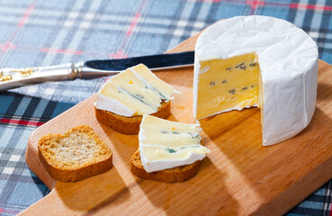 Delicate soft blue cheese served with small slices of toasted bread on wooden cutting board