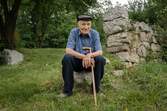 one man senior caucasian male pensioner old farmer standing alone outdoor in the field in backyard by ruined building foundation in summer day looking to the side lonely real people copy space