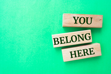 You belong here words on wooden blocks on green background.