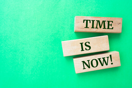 Time is now words on wooden blocks on green background.
