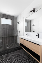 A beautifully renovated bathroom with a wood vanity cabinet, black marble herringbone tiles in the shower, and a white countertop with black faucets. 