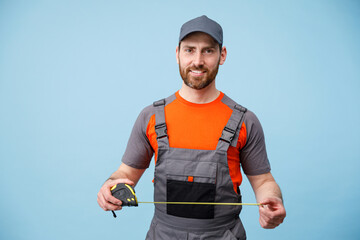 Smiling repairman worker in uniform holding measure tape on yellow studio background