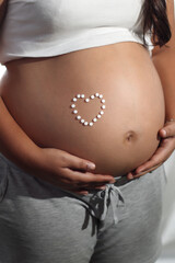 Pregnant woman pill hearth on belly with gray shorts and white shirt