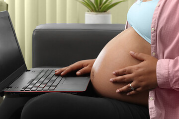 pregnant woman typing on laptop sitting on couch in living room