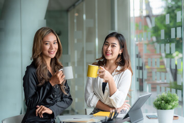 Happy two young Asian business woman holding coffee cup in office.