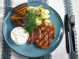 Grilled beef' tongue with potatoes and sour cream on the blue plate 