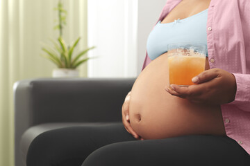 Pregnant woman siting on couch in living room, drinking juice