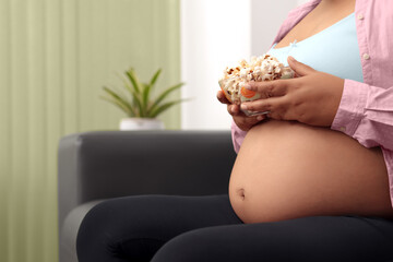 Pregnant woman siting on couch in living room, eating corn pop
