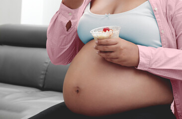 Pregnant woman eating yogurt on couch in living room