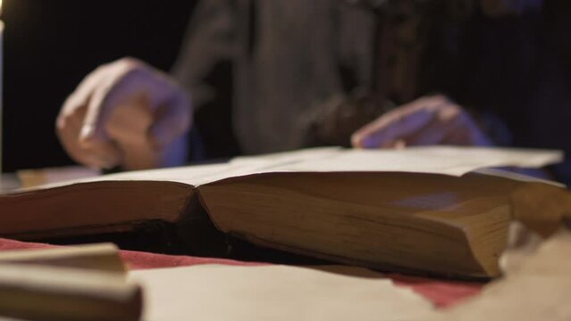 Old ancient book.Historical period reenactment.
Historical era man reading a book by candlelight.
