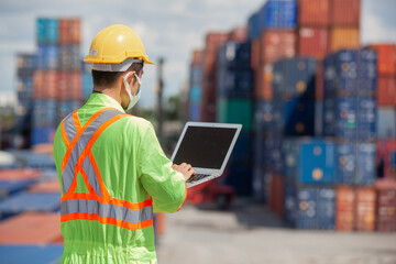 worker standing in shipping container yard holding laptop with smile. Import and export product. Manufacturing transportation and global business concept.