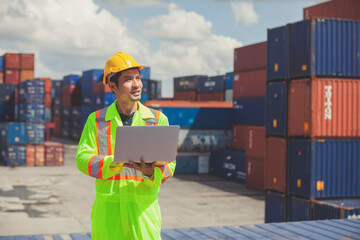 worker standing in shipping container yard holding laptop with smile. Import and export product. Manufacturing transportation and global business concept.