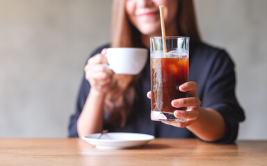 Closeup image of a young woman holding and drinking hot coffee and iced coffee