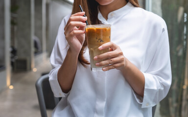 Closeup image of a young asian woman holding and drinking iced coffee