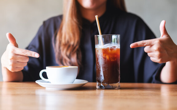 Closeup image of a young woman pointing finger at two glasses of iced coffee and hot coffee