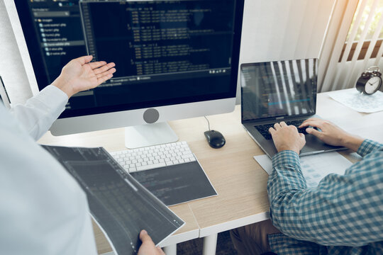 Two software developers are analyzing together about the code written into the program on the computer in office room.