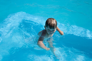 Emotional Toddler baby in the pool playing water toys. A little boy laughs by shooting water from a water gun in the camera.a little boy of 3 years old in an open-air pool with blue water