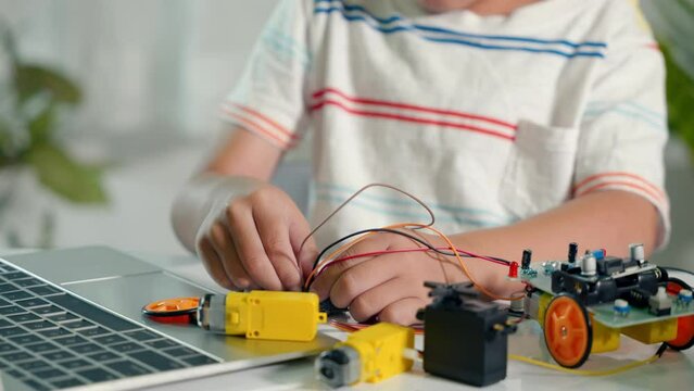Asian kid boy plugging energy and signal cable to sensor chip with Arduino robot car, Little child remotely learn online with car toy, STEAM education AI technology course school learning lesson