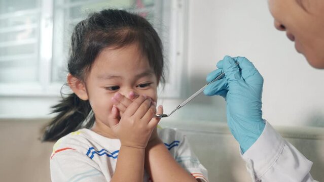 Dental kid examination. Doctor examines oral cavity of child uses mouth mirror to check teeth cavity but little girl cover mouth no need to checking she afraid, scared and closes his mouth with hands
