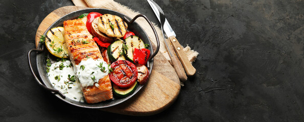 Salmon steak with vegetables and white sauce on dark background.