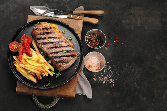 Striploin beef steak with french fries on dark background.