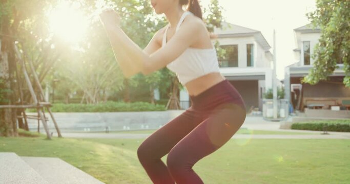 Beautiful young Asia athlete lady exercises doing squat jumps after running on urban stairs at park environment in evening sunset. Outside workout and fitness healthy lifestyle concept.