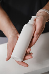 Female hands holding white cosmetic bottle on white background. Skin care, pure beauty, body...