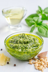 Green fresh homemade italian pesto sauce made of blended basil leaves, olive oil, pine nuts, garlic and parmesan served in transparent glass bowl on white wooden table used in salad or pasta seasoning