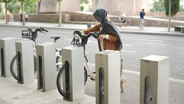 Muslim woman picks up an electric bike parked in the city