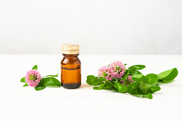 Herbal oil in a brown glass bottle on a white wooden background with meadow clover flowers. Essential oil for spa, massage and alternative medicine.