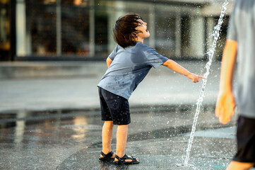 a boy of Asian appearance with long hair in a blue T-shirt is bathing in a fountain on a hot summer...