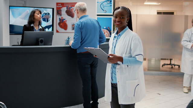 Portrait of african american doctor in hospital reception lobby, analyzing checkup files with appointment to take patient in medical cabinet for consultation. Physician with healthcare expertise. - Powered by Adobe